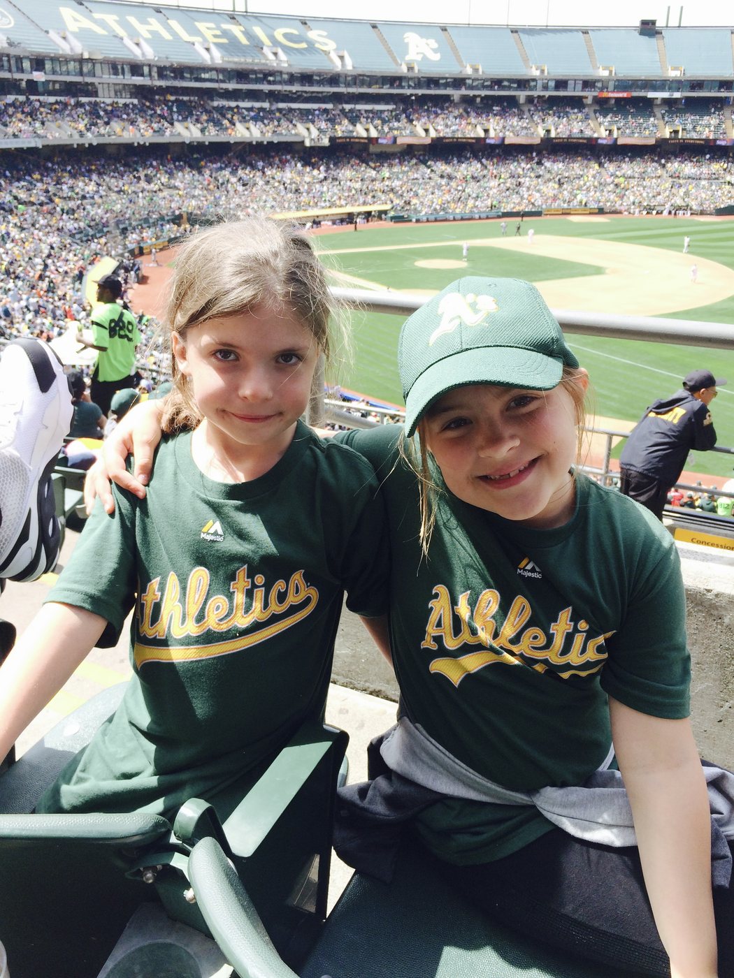 The Clark twins as young girls in green Oakland Athletics shirts, arms around each other at a ballgame