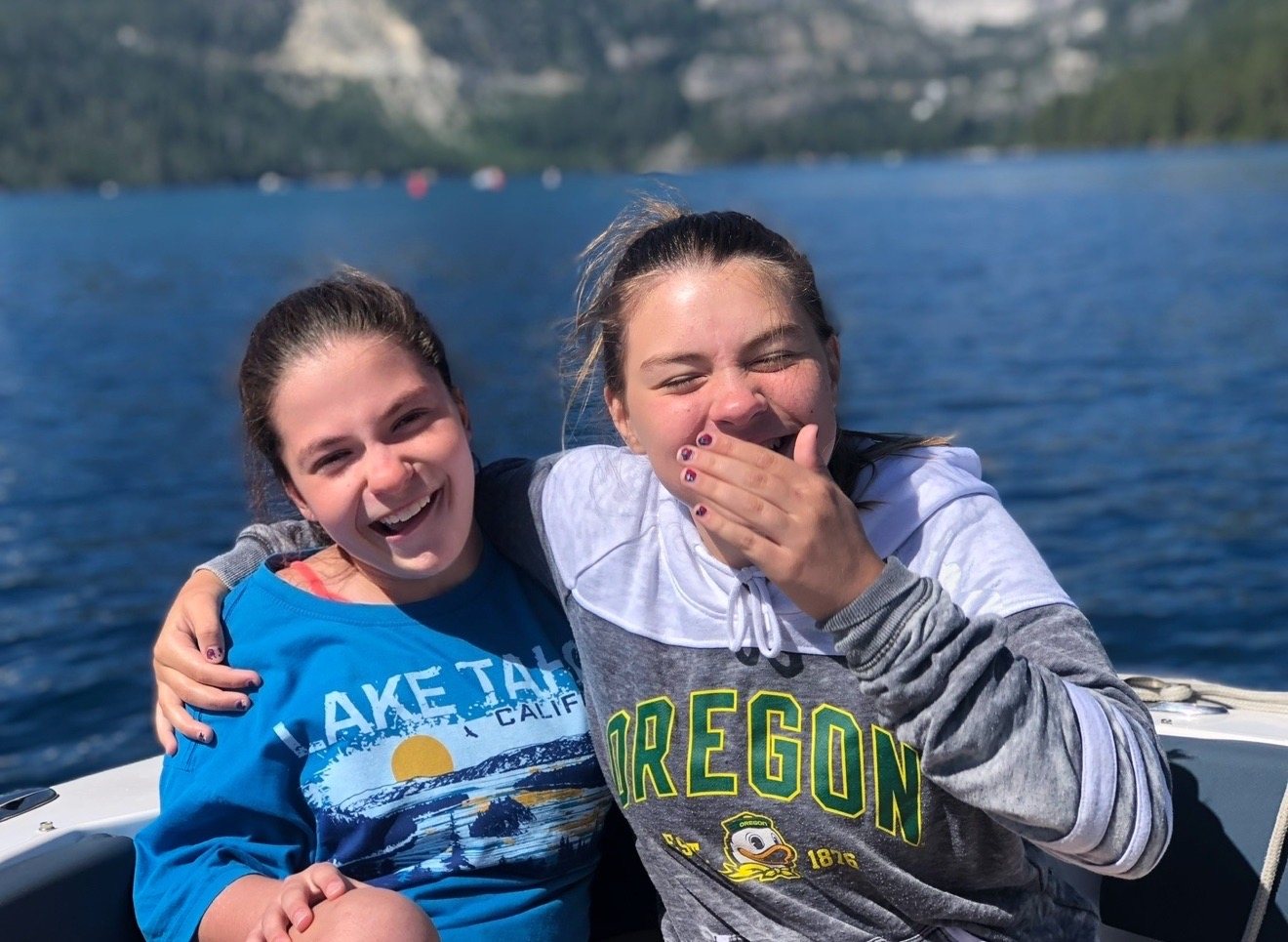 The Clark twins laughing together on a boat at Lake Tahoe, mountains and blue water behind them